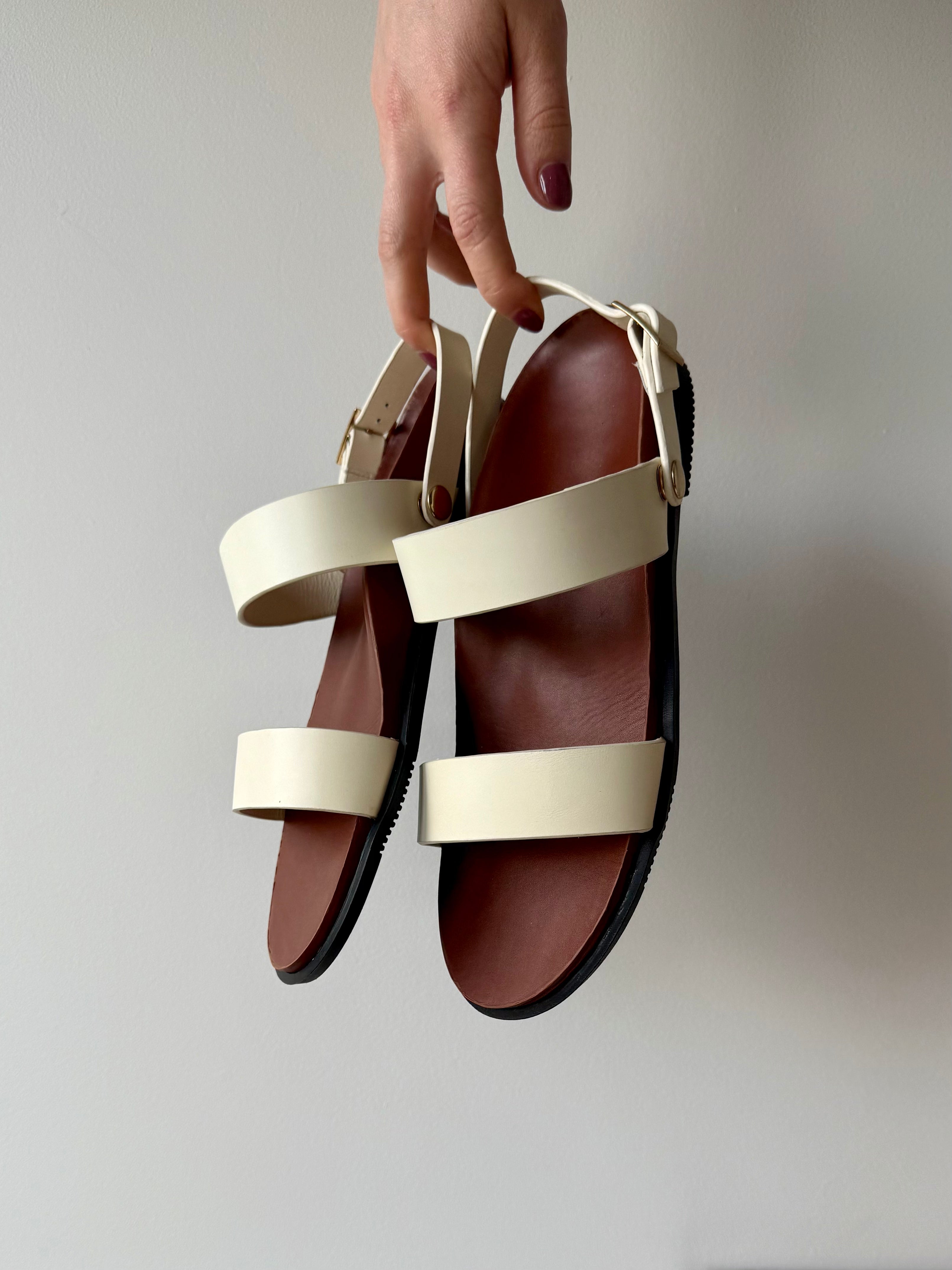 Hand holding white and brown sandals